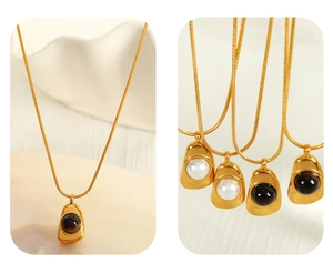Detail of irregular geometric gold necklace with pearl and dark gemstone on snake chain