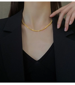Close-up of sparkling gold stardust chain necklace on model wearing a black blazer