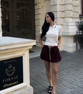 Close-up of a white knit polo shirt and dark purple drawstring skirt set for women