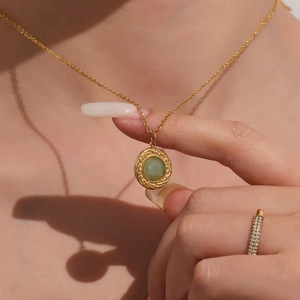 Golden necklace with vintage embossed pendant and green gemstone on female neck