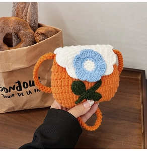 Detail of handmade crochet orange crossbody bag with blue flower and white flap