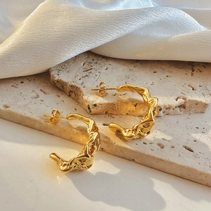 Detail of 18k gold C-shaped earrings with irregular wavy texture on stone and silk