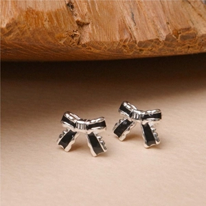 Detail of s925 silver bow stud earrings with black enamel on a warm wood background