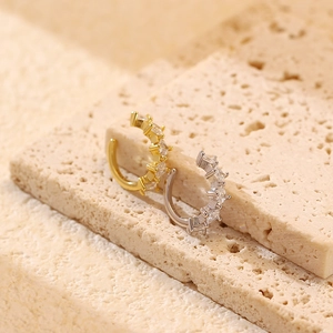 Macro view of C-shaped gold and silver ear cuffs with cubic zirconia on stone base