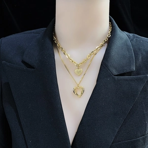 Detail of layered gold necklaces with solid and hollow heart pendants on a black background
