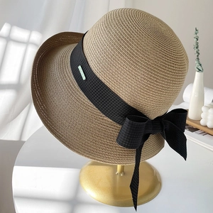 Chapeau de paille beige avec ruban noir et nœud exposé sur un support doré élégant