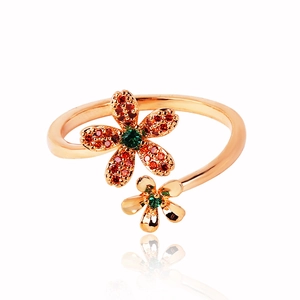 Rose gold flower ring with red and green gemstones on white background with reflection