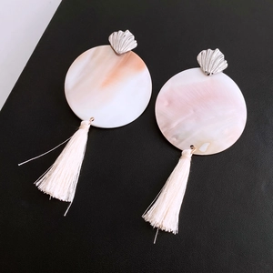 Detail of round shell earrings with peach-white gradient and beige tassels on black leather