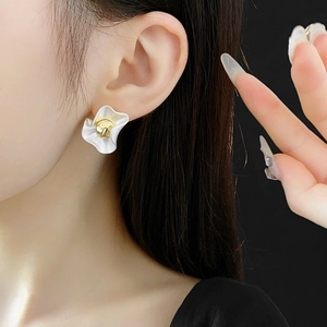 Detailed view of white petal-shaped earrings with a gold center bead on a model