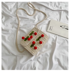 Top view of beige straw woven crossbody bag with cute red cherry accents on white fabric