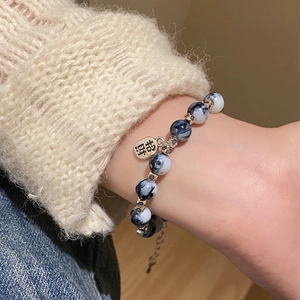 Close-up of pearl and obsidian beaded bracelet with Lucky charm tag on female wrist