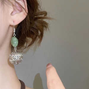 Gros plan des boucles d'oreilles perle verte et sphère évidée argentée sur le modèle