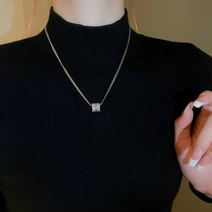 Detail of silver layered zircon cylinder pendant necklace worn on a black knit sweater