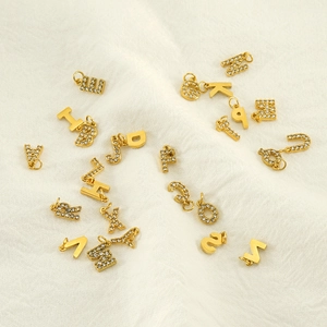 Macro shot of gold-plated alphabet pendants with sparkling rhinestones on white fabric