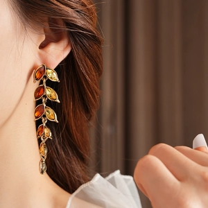 Détail de boucles d'oreilles vintage dorées à pompons et cristaux ambrés sur modèle