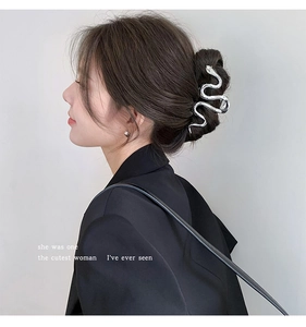 Silver snake-shaped metal hair claw clip worn on a low bun by a woman in a black suit
