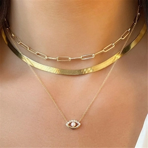 Close-up of triple-layered gold necklaces with pearl devil eye pendant and snake chain