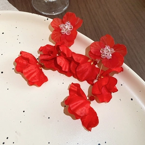 Detail of red fabric flower earrings with beaded center on a cream ceramic plate
