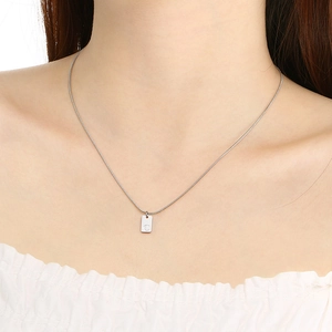 Close-up of a silver rectangular pendant necklace with engraved letter C on a model