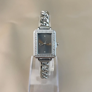 Close-up of a silver rectangular watch with a diamond bezel and grey dial on a stand