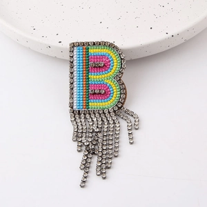 Close-up of rainbow letter B brooch with hanging rhinestone tassels on a white plate