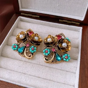 Vintage floral pearl earrings with rhinestones on a dark wood jewelry box surface