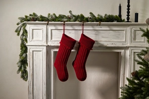 Detail of red knitted Christmas stockings hanging on fireplace with pine branches deco