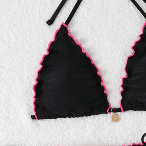 Detail of black bikini top with pink ruffle trim and golden sun pendant on white rug