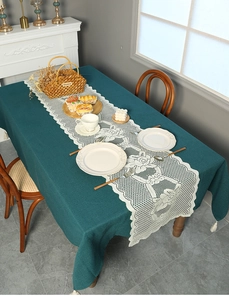 Close-up of white lace table runner with fringe on a dark green tablecloth