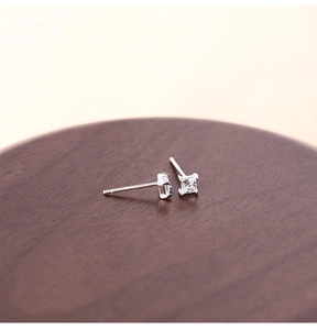 Macro shot of silver square cubic zirconia stud earrings on a dark wood tray
