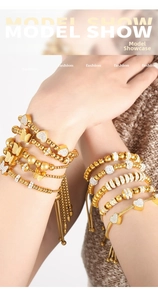 Close-up of layered gold beaded bracelets with heart and butterfly charms on wrist