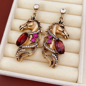Détail de boucles d'oreilles tête de cheval dorées avec pierres rouges et cristaux