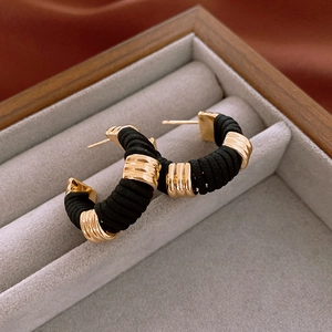 Macro shot of C-shaped earrings with black woven cord and gold metallic accents