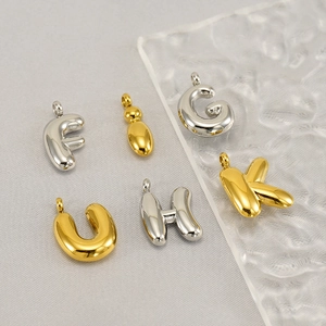Detail of golden and silver bubble letter charms and gourd pendant on textured glass
