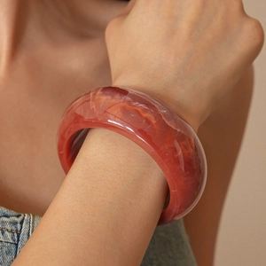 Detail of red translucent resin bangle with unique marble texture worn by a model