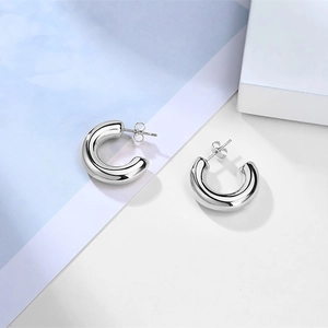 Macro shot of silver-colored hollow C-shaped stud earrings with matching metal butterfly backs