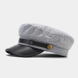 Macro shot of black leather brim with litchi texture and golden button on a grey newsboy cap