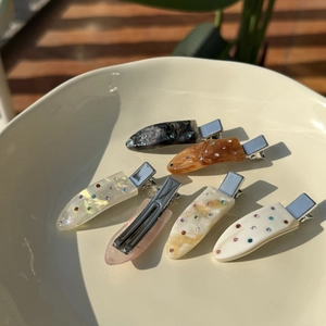 Detailed view of colorful acetate hair clips with crystal inlay on a ceramic plate