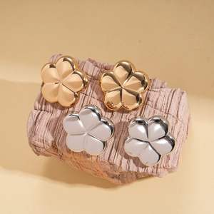 Minimalist polished metal flower stud earrings in gold and silver finishes on wood