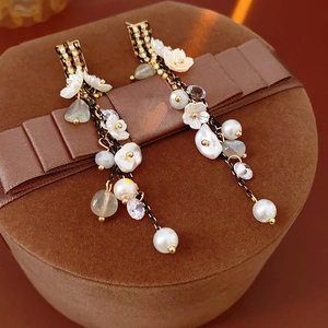 Detail of long fringe earrings with pearls and flower petals on a brown velvet box