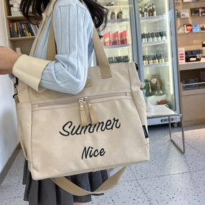 Model wearing large beige canvas tote bag with Summer Nice embroidery in a cafe