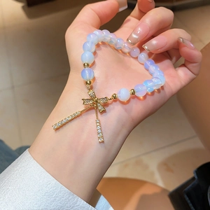 Detail of beaded bracelet featuring light blue cat eye stones and gold zircon bow charm