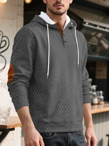 Détail d'un sweat à capuche gris avec texture matelassée et patchs aux coudes contrastés