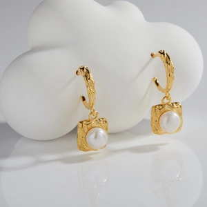 Detail of gold drop earrings with irregular hammered metal and white round pearl inserts