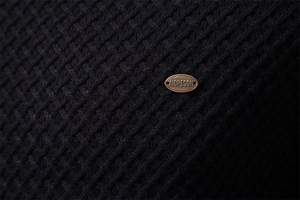 Macro detail of dark knit fabric texture and premium bronze metal logo on men's sweater