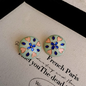 Detail of round mint green enamel earrings with pink heart and blue flower patterns