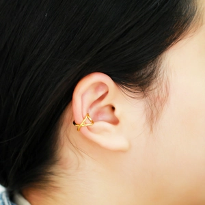 Detailed view of a gold criss-cross ear cuff on model without ear piercing