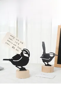 Detail view of two minimalist metal bird memo holders on light natural wood bases