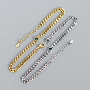 Detailed macro view of gold and silver tank chain bracelets with green round gemstones