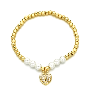 Golden beaded bracelet with pearls and a crystal heart pendant on white background